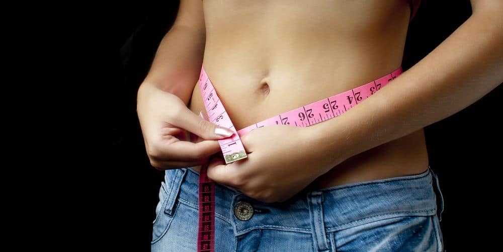 Woman measuring stomach to show weight loss